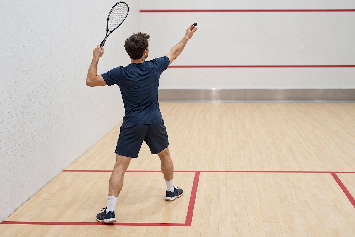 Squash player preparing an overhead serve with a raised racket on an indoor court