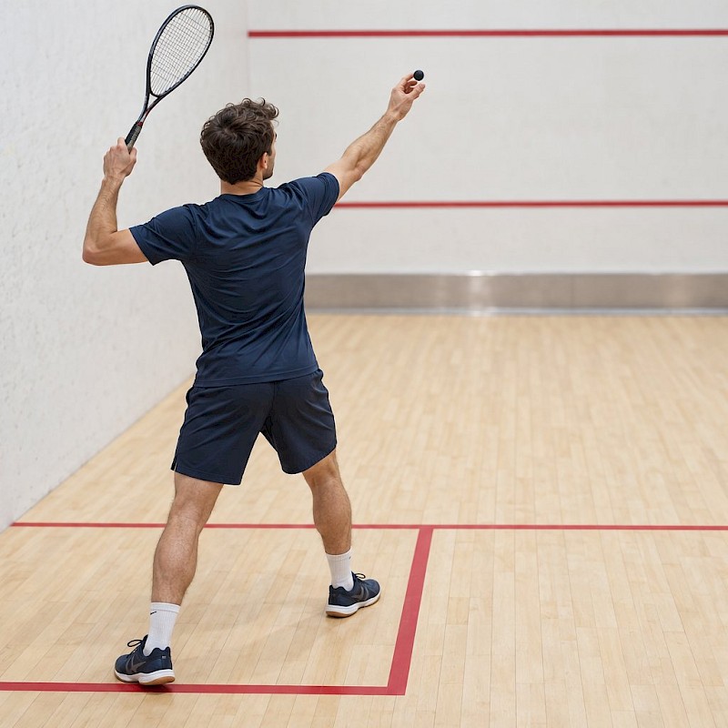 Squash player preparing an overhead serve with a raised racket on an indoor court