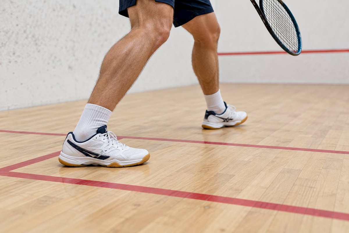 Court shoes positioned inside a squash service box, clear of the red boundary line