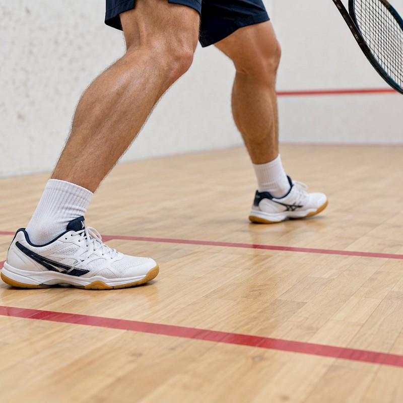 Court shoes positioned inside a squash service box, clear of the red boundary line