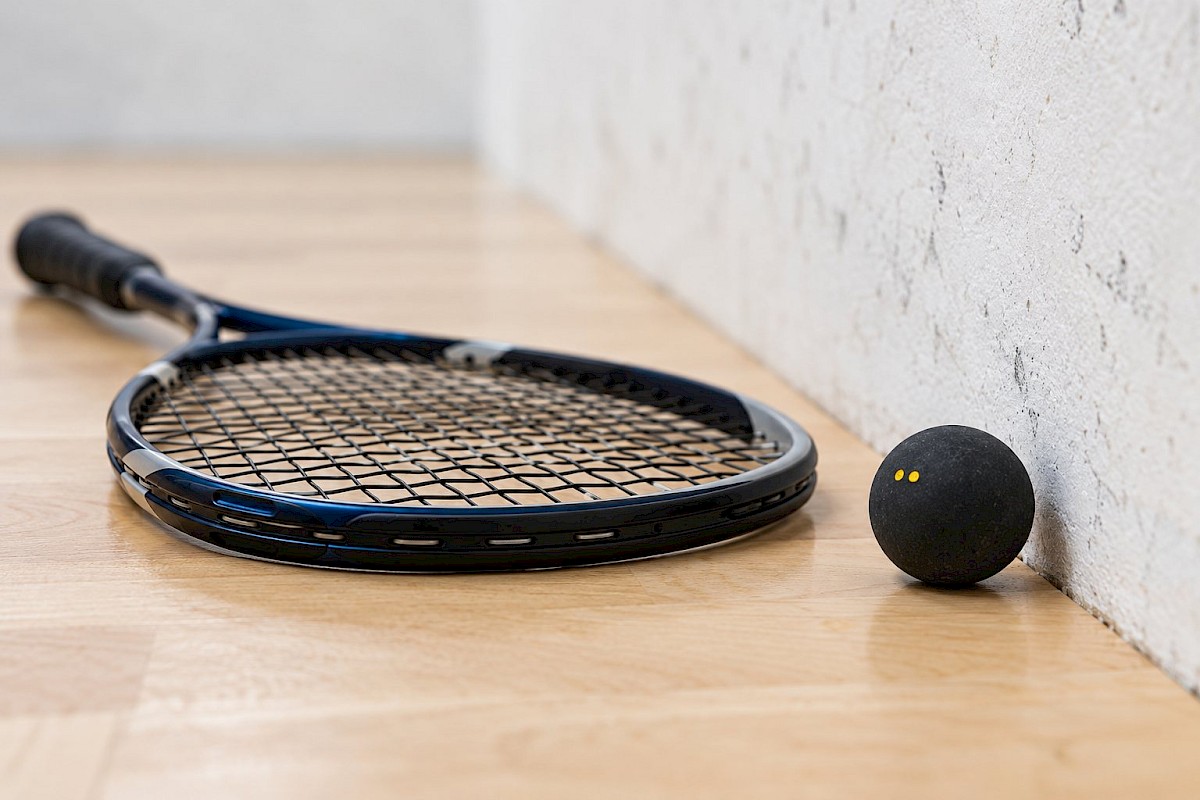 Squash racket and small double-yellow-dot ball beside a court side wall