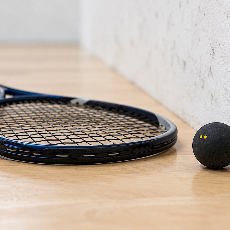 Squash racket and small double-yellow-dot ball beside a court side wall