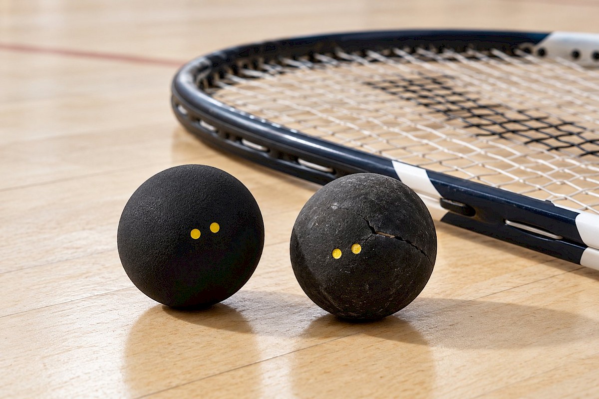 A new squash ball beside a worn ball with a small split in its rubber